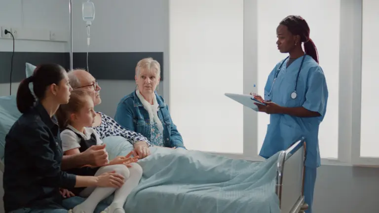 A nurse talking with an older man and his family beside his hospital bed.
