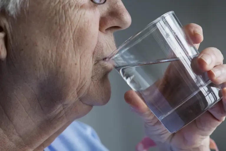 An older woman drinking a glass of water.