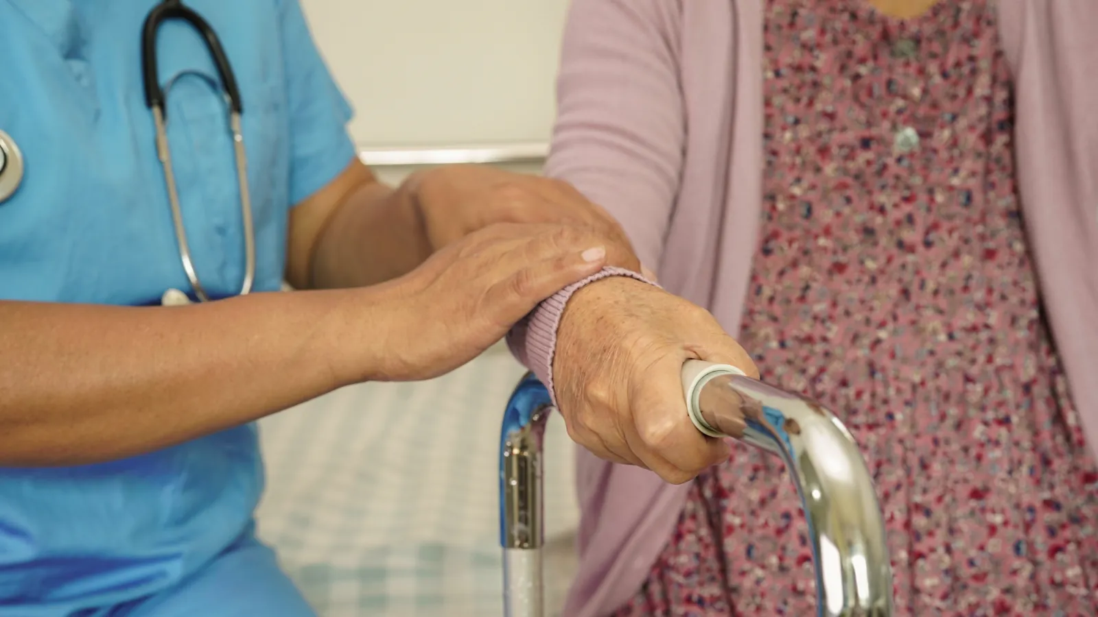 A care worker supporting a person’s forearm beside a walking frame.
