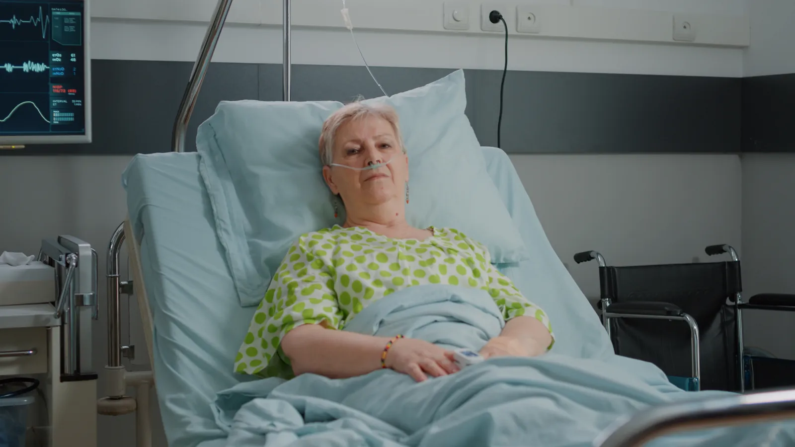 An older woman with nasal oxygen lies still in a hospital bed.